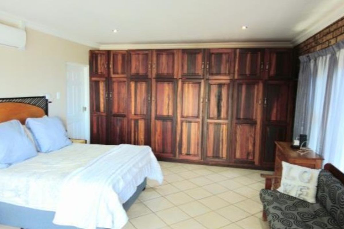Spacious bedroom featuring extensive built-in wooden cabinetry, tiled flooring, an air conditioning unit, and an exposed brick feature wall.