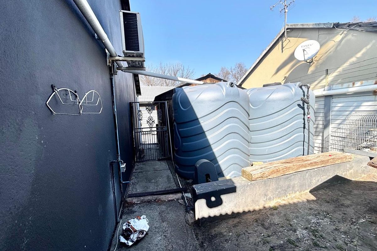 Rear exterior area featuring two large water storage tanks, an air conditioning condenser unit, and a secure gated access point.