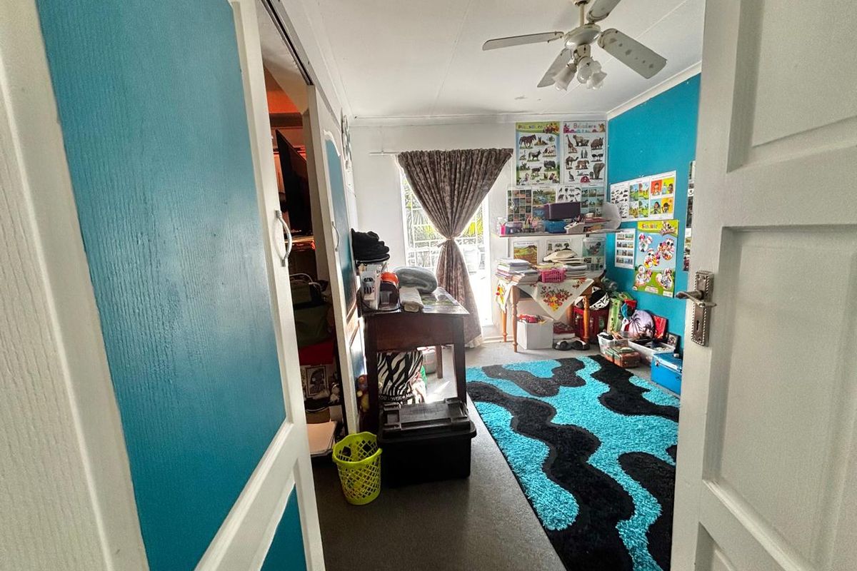 A bedroom featuring a ceiling fan, built-in storage, and a sliding door leading to an outdoor area, currently used as a study or play space.