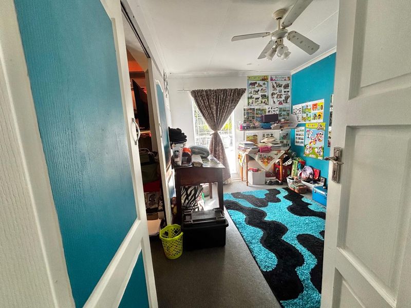 A bedroom featuring a ceiling fan, built-in storage, and a sliding door leading to an outdoor area, currently used as a study or play space.