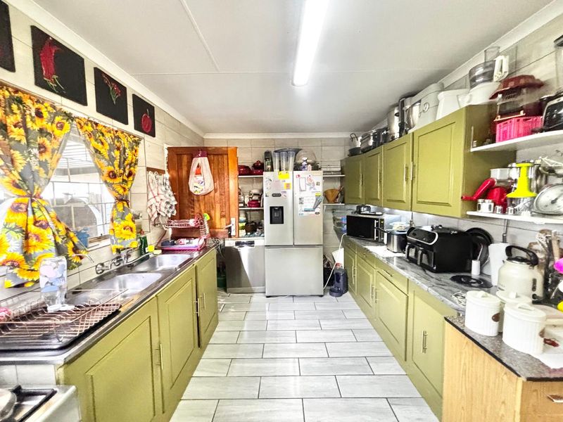 A functional galley-style kitchen featuring olive green cabinetry, double basin sink, and tiled flooring, offering ample storage and workspace.