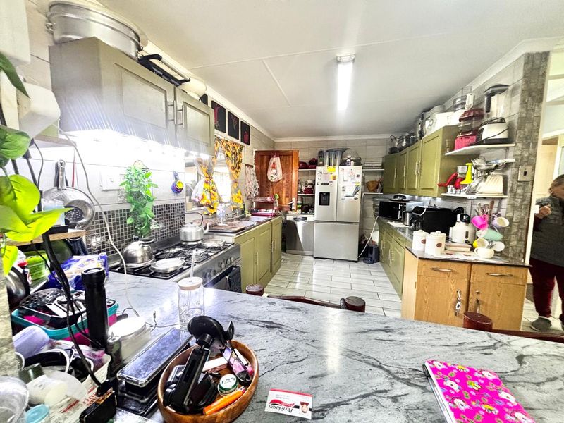 A functional kitchen featuring stone countertops, gas hob with extractor, tiled backsplash, and ample built-in cabinetry with a tiled floor finish.