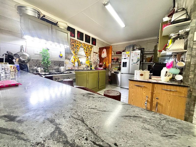 A functional kitchen featuring granite countertops, built-in cabinetry, and a gas stove with an extractor fan, offering a practical layout for daily cooking.