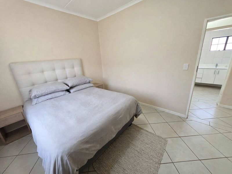 A bedroom featuring neutral wall tones and tiled flooring, with an adjoining bathroom visible through the doorway.