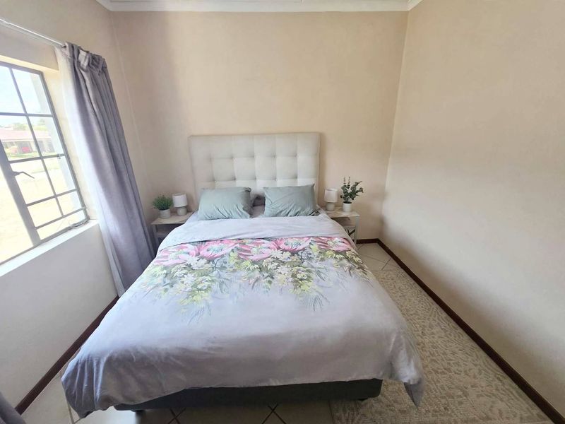 A compact bedroom featuring tiled flooring and a window fitted with security bars, providing a functional and neutral living space.
