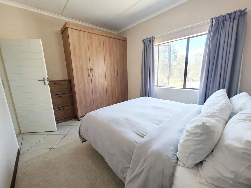 A well-maintained bedroom featuring neutral wall tones, tiled flooring, and a large built-in wardrobe with ample storage space.