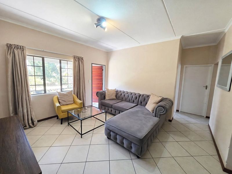 A bright living room featuring tiled flooring, neutral wall finishes, and a window with security bars, providing a functional and well-lit living space.