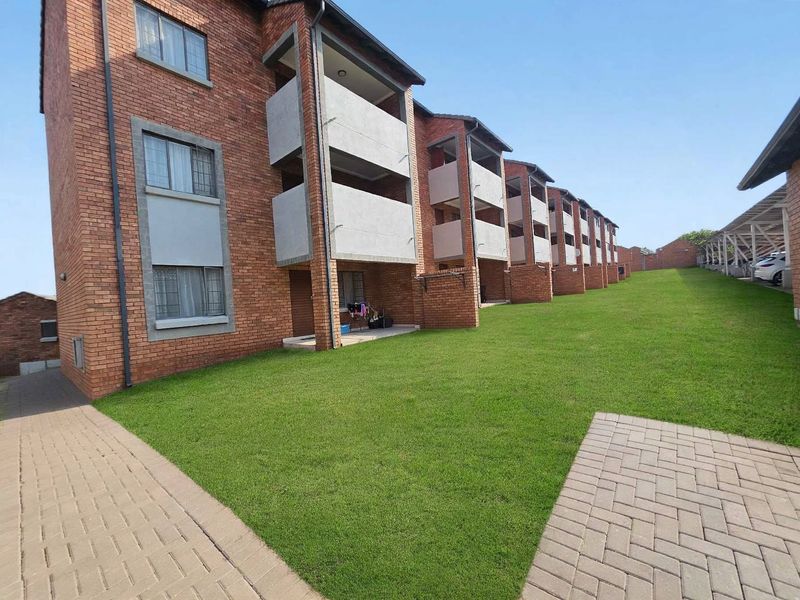 A view of the rear elevation of a multi-story apartment complex featuring face brick construction, private balconies, and well-maintained communal lawn areas.