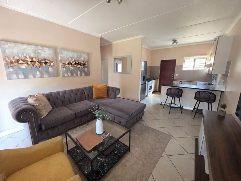 Open-plan living area featuring tiled flooring, a functional kitchen with breakfast bar, and neutral wall finishes.