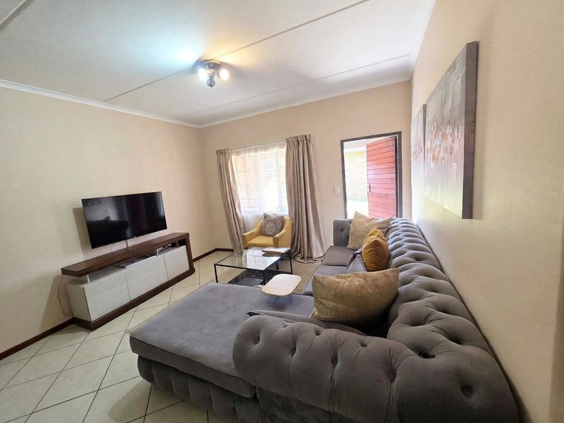 A comfortable living room featuring tiled flooring, neutral wall tones, and direct access to an exterior entrance.