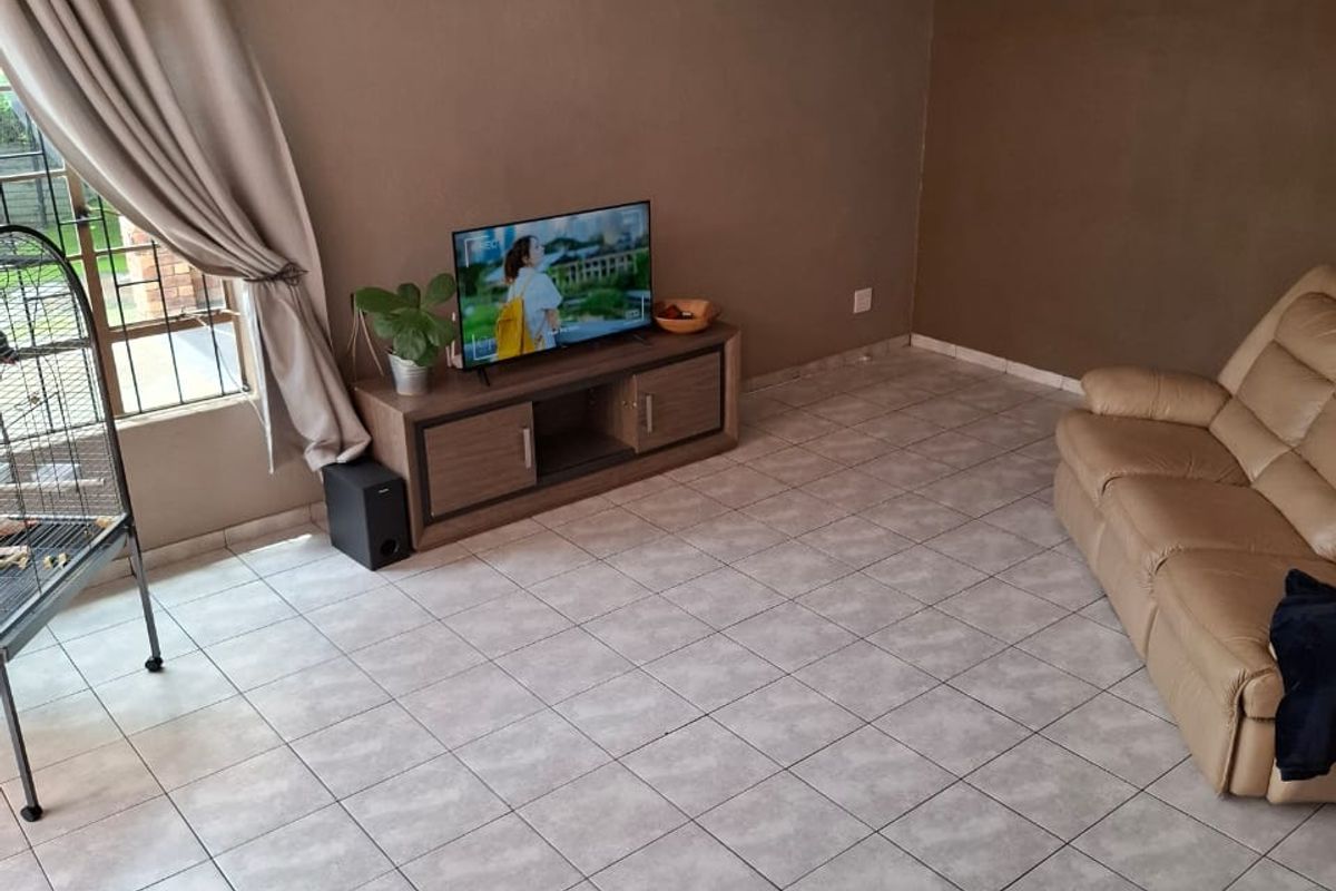 A living room featuring ceramic floor tiles, a ceiling fan, and a window, providing a functional space with neutral wall tones.
