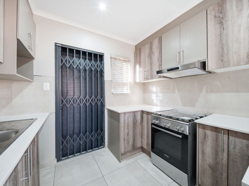 Modern kitchen featuring wood-look cabinetry, stone countertops, stainless steel appliances, tiled flooring, and a secure metal gate leading to the exterior.