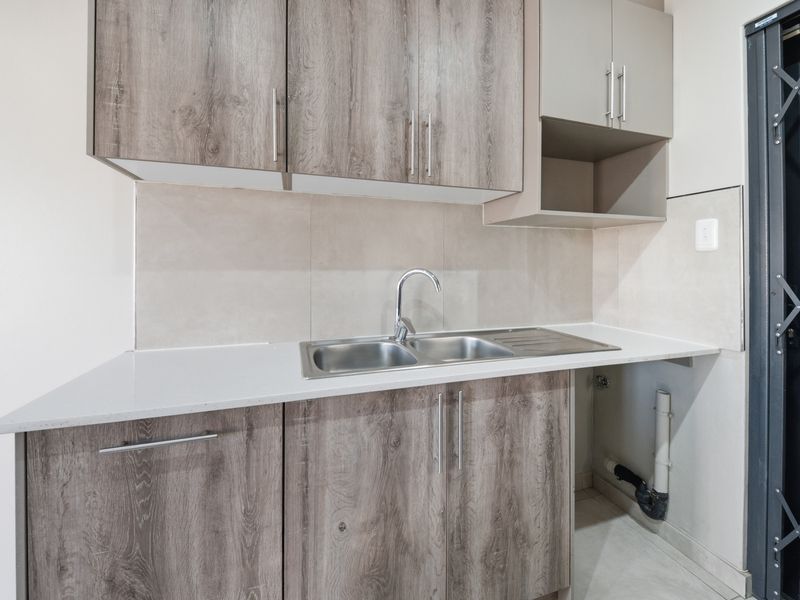 A clean and functional scullery area featuring modern wood-look cabinetry, a stainless steel sink, and stone countertops with a tiled splashback.