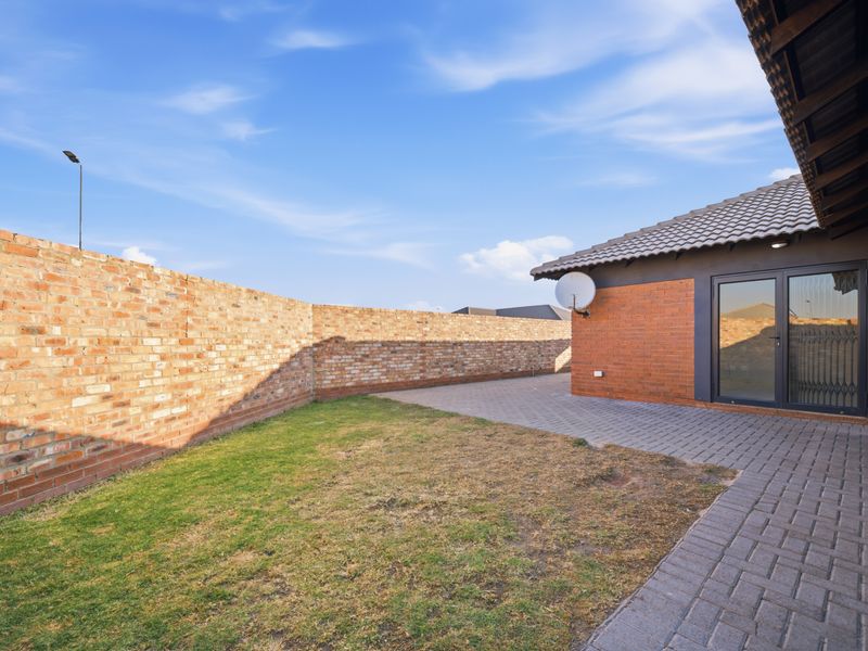 A private rear garden featuring a paved patio area, brick boundary wall, and direct access to the home via a sliding glass door.