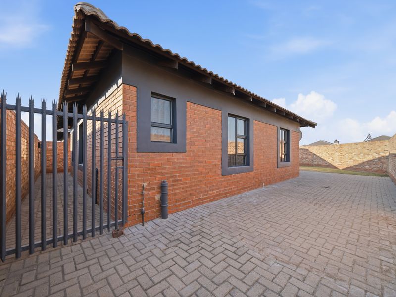 A well-maintained rear exterior view of the house featuring exposed brickwork, a tiled roof, paved courtyard, and secure perimeter walling.