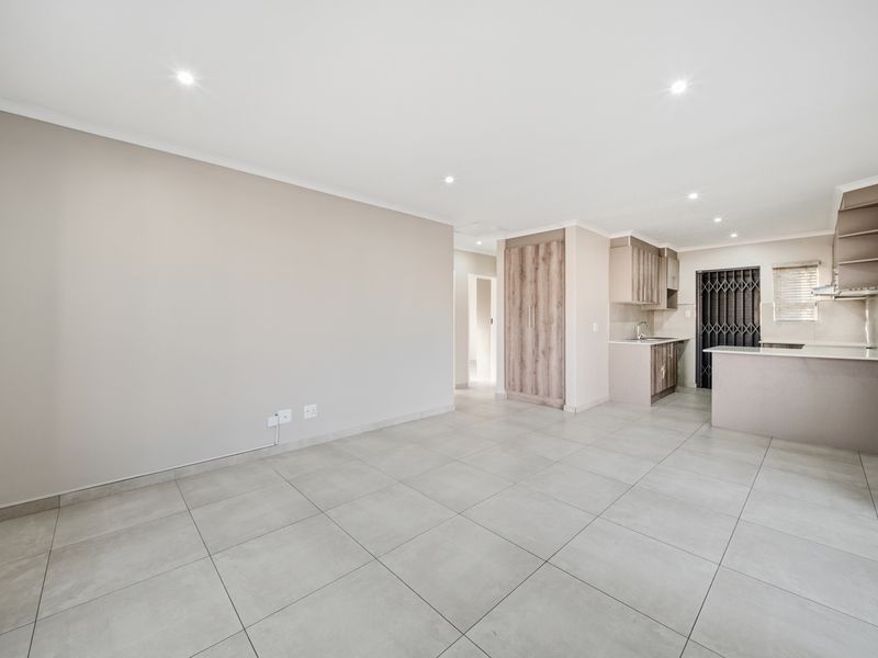Spacious open-plan living area featuring neutral tiled flooring, recessed lighting, and a modern kitchen with built-in cabinetry and a breakfast island.