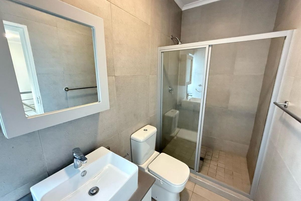 A modern, clean bathroom featuring a glass-enclosed shower, a contemporary ceramic basin, a toilet, and neutral wall tiling.