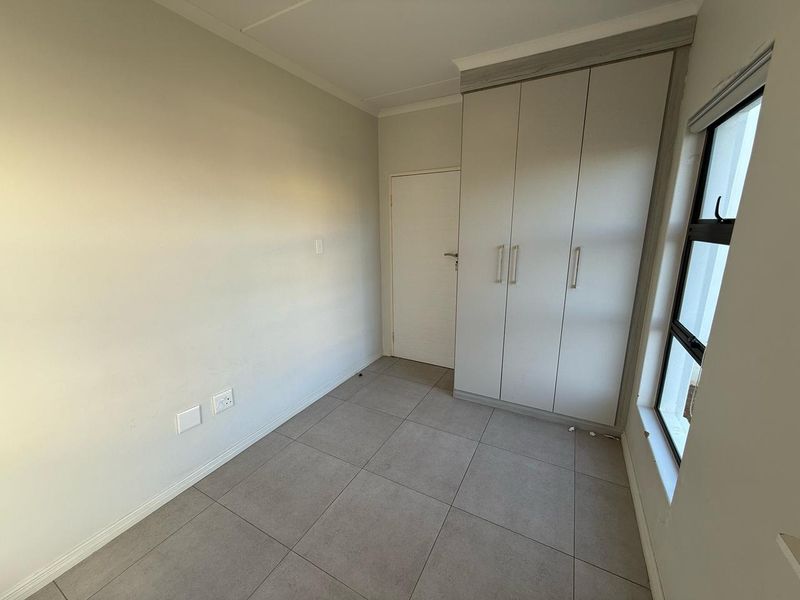 A clean, empty bedroom featuring neutral tiled flooring, built-in cupboards, and a large window providing natural light.