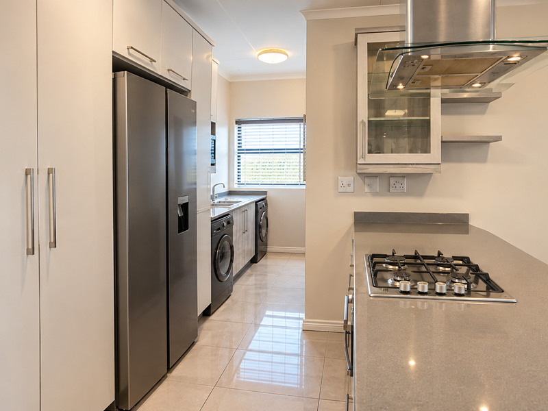 Modern kitchen featuring stone countertops, a gas hob with extractor fan, ample built-in cabinetry, and sleek tiled flooring, leading into a functional laundry area.