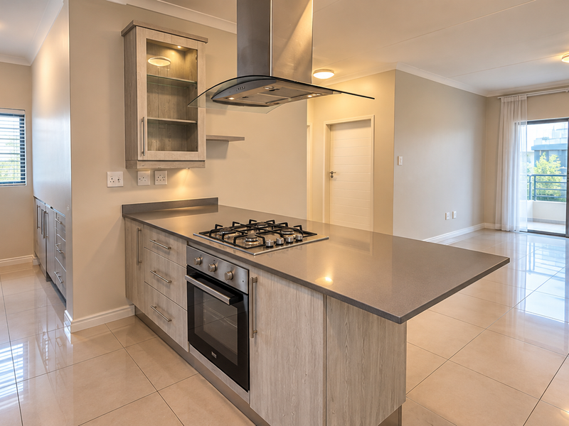 Modern open-plan kitchen featuring stone countertops, built-in gas hob, oven, and extractor fan, flowing into a bright living area with access to a balcony.