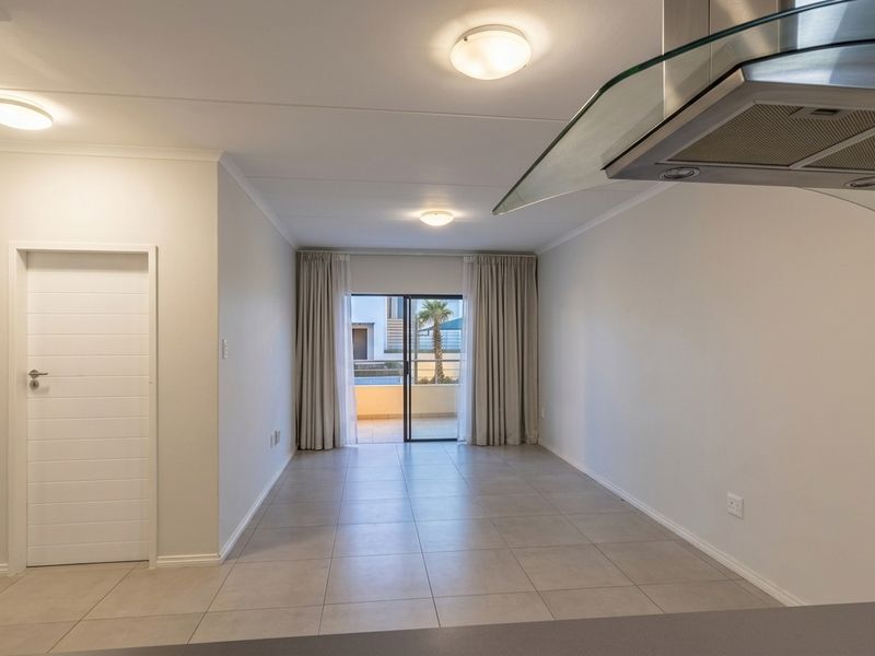 An open-plan living area featuring neutral tiled flooring, modern ceiling lighting, and a sliding glass door leading to an outdoor balcony.