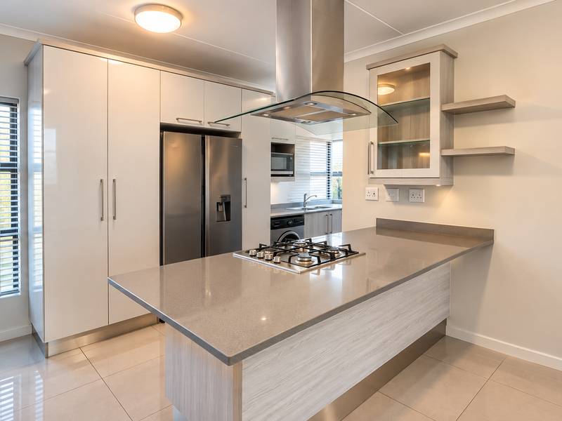 Modern kitchen featuring sleek white cabinetry, stone countertops, a gas cooktop with a stainless steel extractor fan, and high-quality tiled flooring.