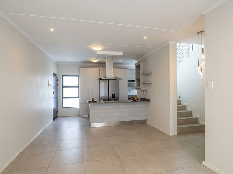Modern open-plan living area featuring a sleek kitchen with island, built-in cabinetry, and tiled flooring, adjacent to a staircase leading to the upper level.