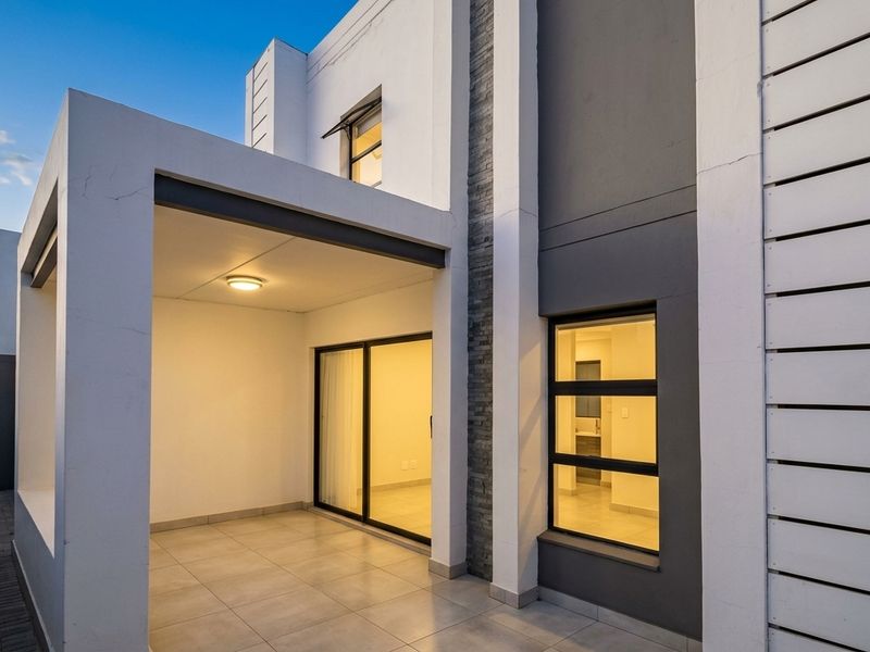 A modern covered patio area featuring tiled flooring, recessed lighting, and a stylish stone-clad feature wall, providing seamless access to the interior living space.