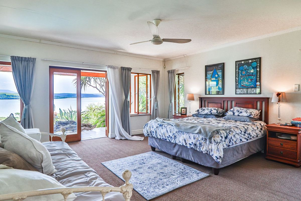 Spacious bedroom featuring carpeted flooring, a ceiling fan, and sliding glass doors opening to a patio with scenic water views.