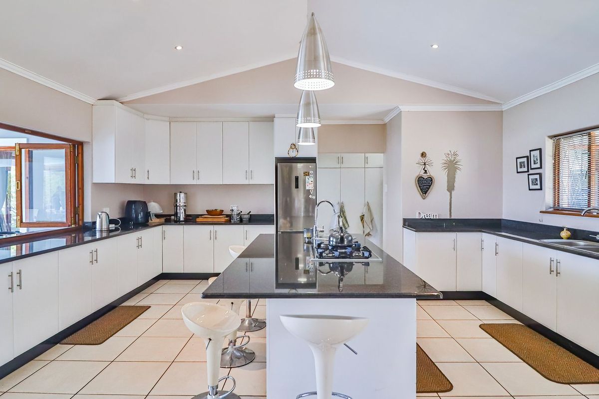 Spacious kitchen featuring white cabinetry, dark granite countertops, a central island with a built-in gas hob, and tiled flooring under a vaulted ceiling.