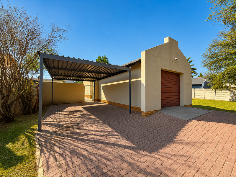 A well-maintained garage featuring a covered carport, a secure roller shutter door, and a neat paved driveway area.