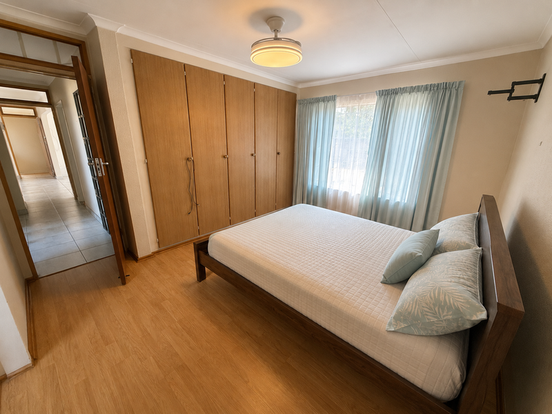 A well-maintained bedroom featuring built-in wooden cupboards, laminate flooring, and a ceiling fan, offering a functional and comfortable living space.