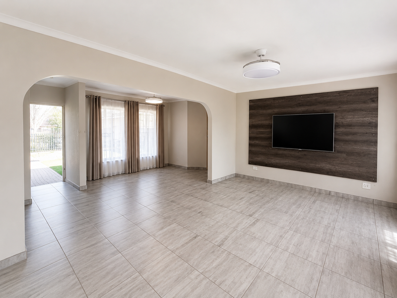 Spacious, light-filled living area featuring neutral tiled flooring, a decorative wood-look feature wall, and an open-plan layout with an arched transition to the entrance.