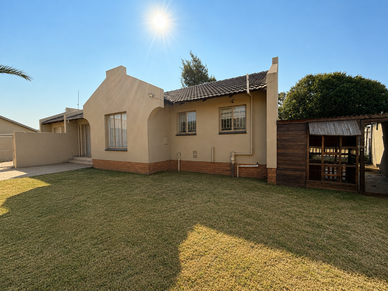 Rear view of the house featuring a paved patio area, well-maintained lawn, and secure window bars.