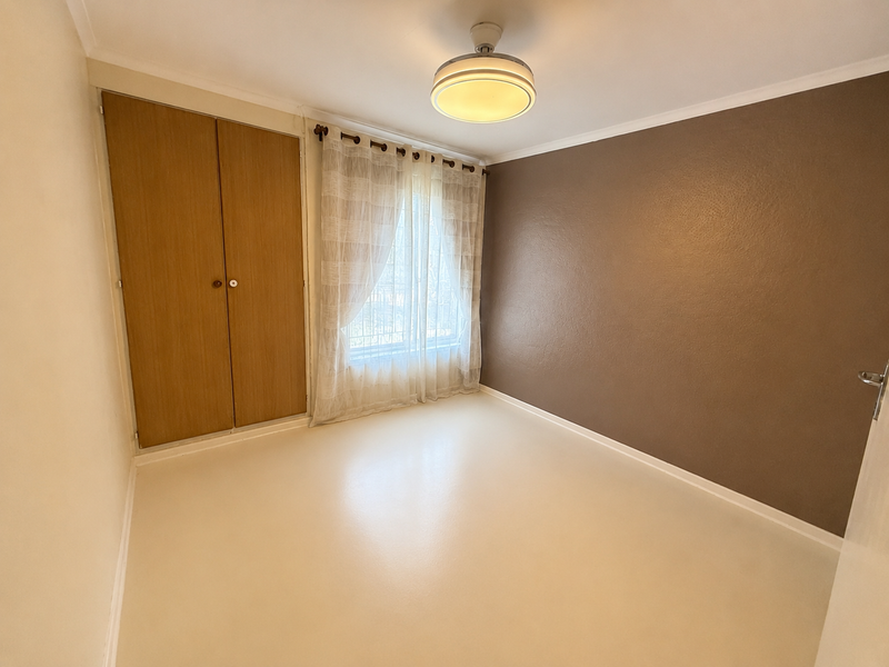 A clean, empty bedroom featuring a built-in wardrobe, neutral flooring, and a feature wall, offering a blank canvas for personalization.