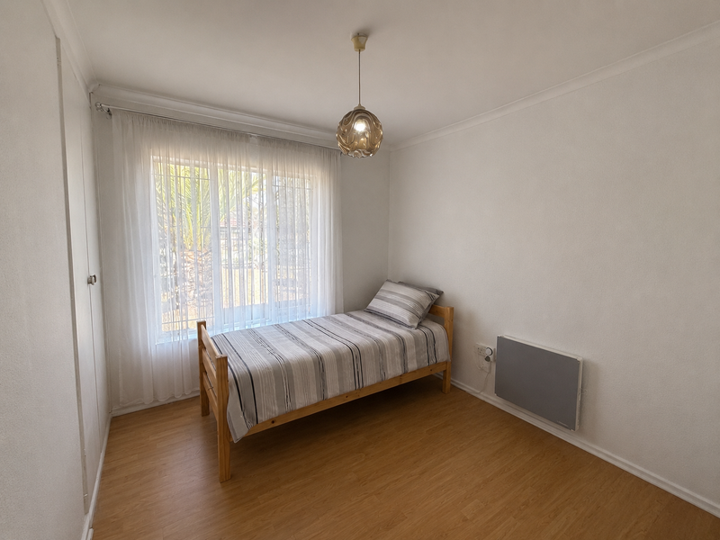 A clean and functional bedroom featuring laminate flooring, a built-in wardrobe, and a wall-mounted electric heater for climate control.