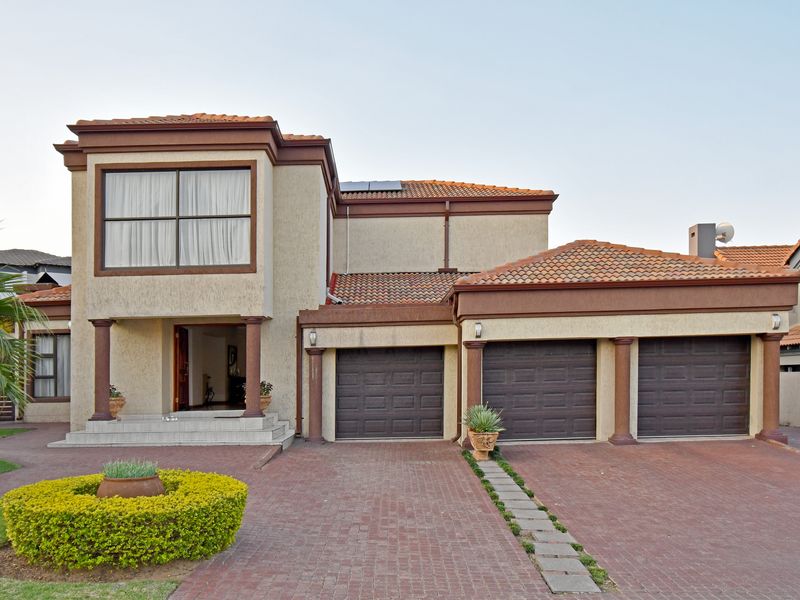 A well-maintained double-story residence featuring a triple garage, paved driveway, decorative columns, and a classic tiled roof facade.