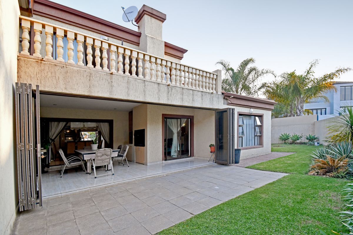 Rear view of the house featuring a tiled patio, built-in braai, folding doors leading to the interior, and a well-maintained garden.