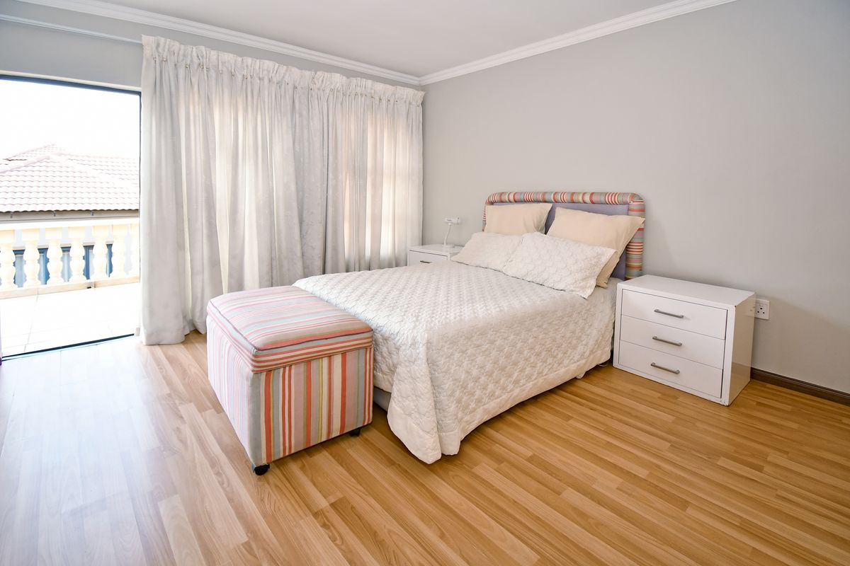A well-maintained bedroom featuring laminate flooring, crown molding, and a sliding glass door providing access to an outdoor balcony.