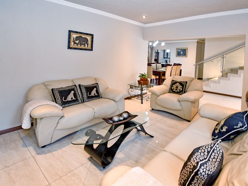 Spacious open-plan living area featuring tiled flooring, recessed lighting, and a modern glass balustrade staircase leading to the upper level.