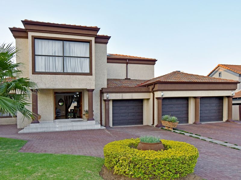 A well-maintained double-story residence featuring a triple garage, paved driveway, and an inviting covered entrance with decorative columns.