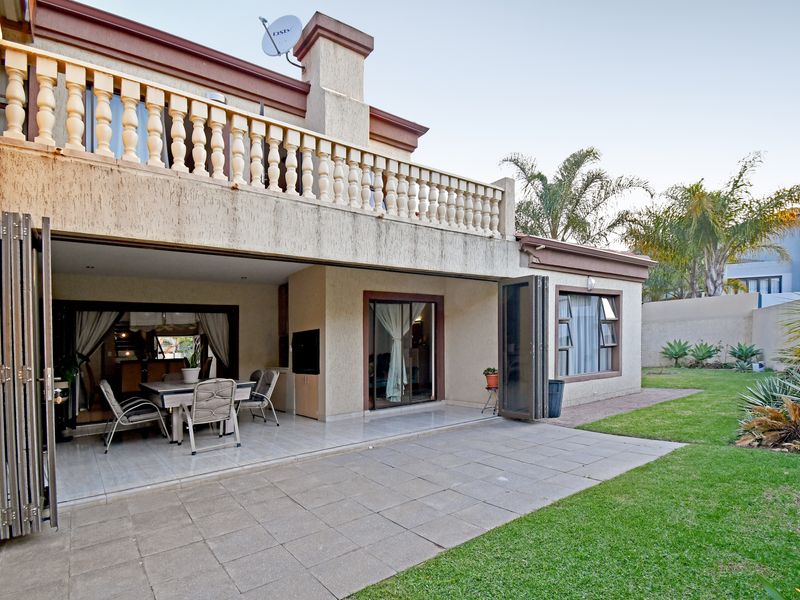 Rear view of the house featuring a tiled patio, built-in braai, folding doors leading to the interior, and a well-maintained garden.