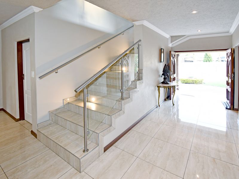 Spacious entrance hall featuring a modern tiled staircase with a glass balustrade, stainless steel handrail, and polished porcelain floor tiles leading to the exterior.