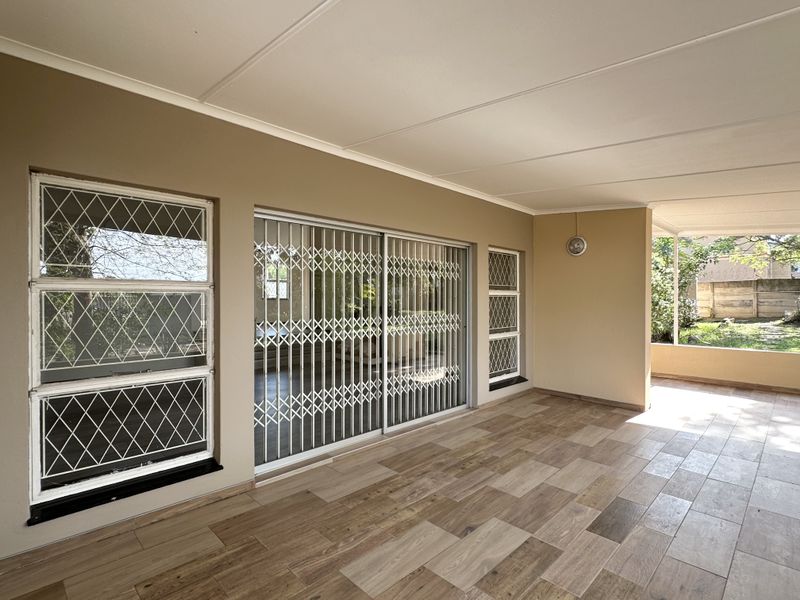 A spacious covered patio featuring wood-look tiled flooring, secure sliding glass doors, and large windows, offering a clean and well-maintained outdoor living space.