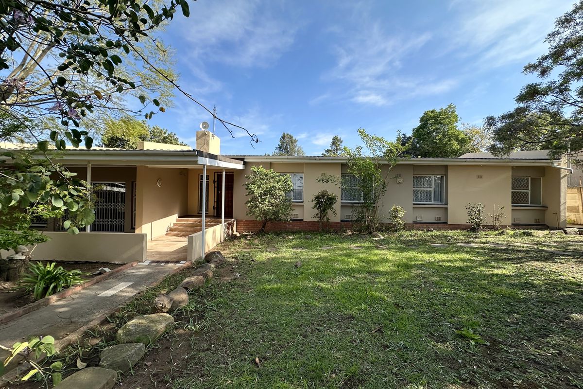 Rear view of the house featuring a covered patio, security gates, and a spacious garden area with a paved walkway.