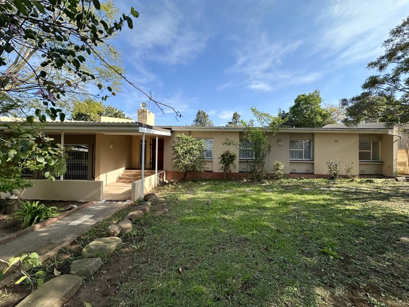Rear view of the house featuring a covered patio, security gates, and a spacious garden area with a paved walkway.