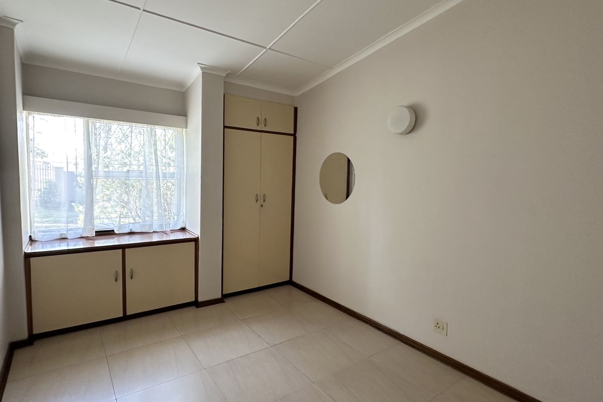 A clean, empty bedroom featuring neutral tiled flooring, built-in cupboards, and a functional window-side storage unit, offering a blank canvas for personalization.