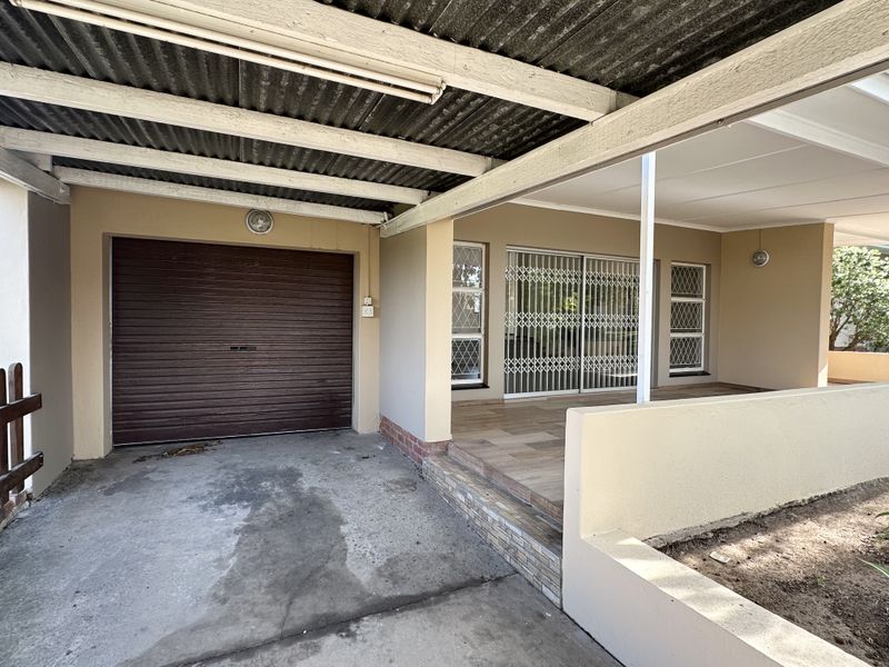 Front exterior view featuring a covered carport, garage door, and a tiled patio area with security gates.
