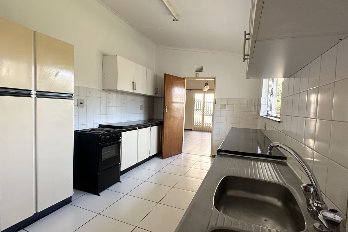 A functional kitchen featuring tiled flooring, built-in cabinetry, a stainless steel sink, and a tiled splashback, offering a clean and practical workspace.