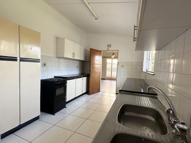 A functional kitchen featuring tiled flooring, built-in cabinetry, a stainless steel sink, and a tiled splashback, offering a clean and practical workspace.